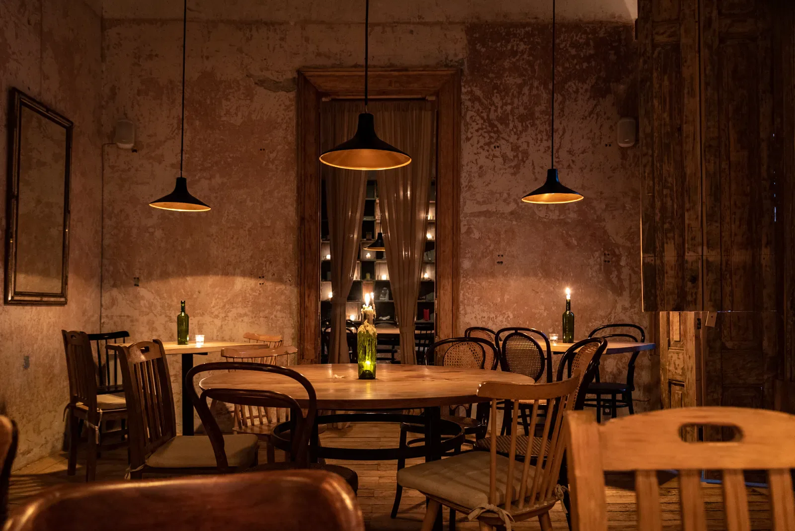 Comedor de Taverna con muros de pátina, mesas de madera y lámparas encendidas.